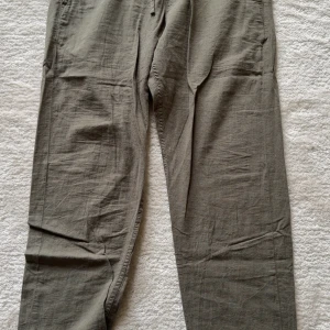 Gröna linnebyxor relaxed fit - Snygga gröna linnebyxor med relaxed fit och rak passform. Byxorna har en avslappnad look och är perfekta för dig som gillar en chill och luftig stil. Tillverkade i linne för en skön känsla och andningsförmåga.