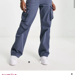 Bershka – Grafitblå cargobyxor med raka ben - Säljer ett par grå cargopants med raka ben och stora fickor på sidorna. Byxorna har en avslappnad passform och är tillverkade i bomull, perfekta för en chill och streetig look. Passar dig som gillar praktiska detaljer och vill ha en cool vardagsstil.