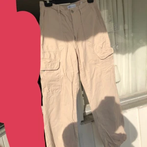 Beige cargobyxor  -  Ett par beige cargobyxor flera stora fickor på sidorna. Byxorna har en avslappnad passform och är tillverkade i bomull. 