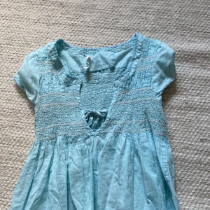 Ljusblå blus från Odd Molly - Supersöt ljusblå blus från Odd Molly med smockdetaljer över bröstet, korta ärmar och knytning vid v-ringningen. Blusen har broderade detaljer och ett luftigt, flowy tyg som känns perfekt för varmare dagar. Använd endast 3 gånger och utan skavanker❤️