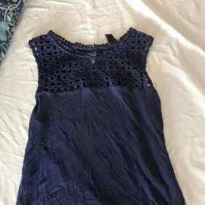 Mörkblå ärmlös blus med spetsdetaljer - Supersnygg mörkblå blus med ärmlös design och broderad spets upptill. Knäppning med knapp i nacken. Jag har sytt om den så den sitter lite tajtare mot kroppen men har inte klippt än så vill man ha den pösigare går det att sprätta upp och vill man kan jag sy in den mer om man vill ha den tajtare. Jag har en vit också om man vill ha den istället💓 Man tänker inte på att jag har sytt inte den själv när den är på! skriv om man vill veta mer 💓