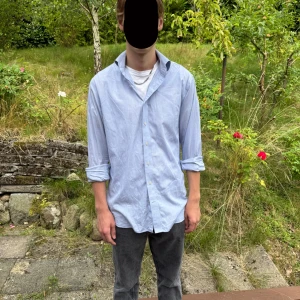 Ljusblå skjorta från Linnéa Braun  - Snygg ljusblå skjorta från The Shirt Factory, designad av Linnéa Braun. Skjortan har extra slim fit, diskreta tunna ränder, klassisk krage och knäppning framtill. Perfekt för dig som gillar stilrena och fräscha plagg. Skulle rekommendera för dig som för M eller L 