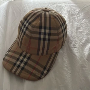 Burberry rutig keps i beige och svart - Snygg keps från Burberry en klassisk model, köpte den för cirka ett halvår sen och den är i bra skick, har du fler frågor om den så e de ba o skicka!