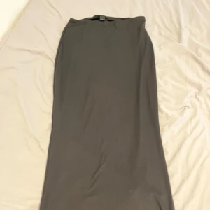 Svart ribbad långkjol - En svart, ribbad långkjol med enkel och stilren design. Kjolen har en rak passform och är gjord i ett stretchigt material som sitter snyggt på kroppen. Perfekt att styla med en crop top eller oversized hoodie.