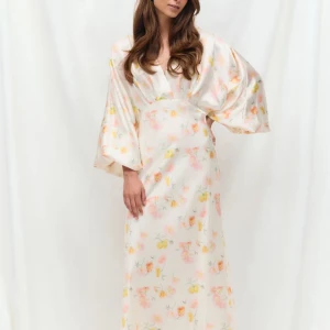 Blommig långklänning i sidenlook - Superfin långklänning med vackert blommigt mönster i pastellfärger på ljus botten. Klänningen har vida ärmar, djup v-ringning och en flowy passform. Materialet har en lyxig sidenkänsla och ger en elegant vibe. Perfekt för dig som vill sticka ut med en romantisk look.