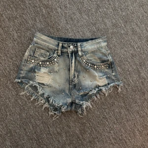 Jeansshorts med nitar och fransar - Snygga ljusblå jeansshorts med slitna detaljer, fransig kant och coola nitar och fransar. 