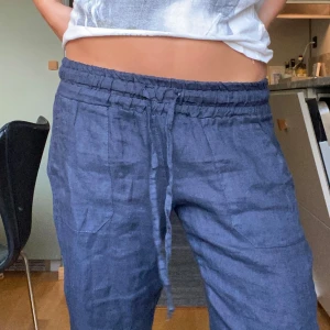 Mörkblå linnebyxor från Chelsea Girls - Snygga mörkblå linnebyxor från Chelsea Girls med avslappnad passform. Byxorna har resår och snörning i midjan samt stora fickor framtill. Perfekta för en chill och stilren look, tillverkade i Italien i mjukt linnematerial. Helt nyköpta, nypris 700kr