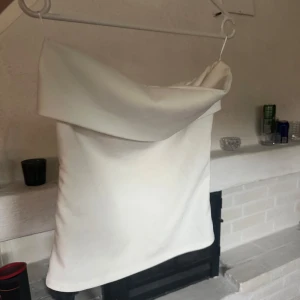 Vit axelbandslös tubtopp med dragkedja - Säljer en stilren vit tubtopp med bred, vikt kant upptill och dragkedja längs sidan.