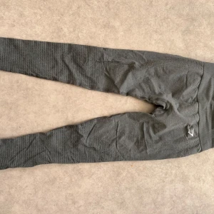 Grå seamless leggings från ICANIWILL - Mörkgrå seamless leggings från Gymshark med hög midja och tight passform. Byxorna har ventilerande mesh-detaljer längs benen och en diskret logga på höften. Perfekta för träning eller chill dagar.