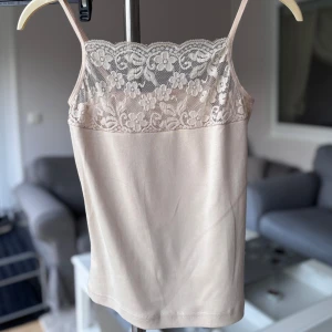 Linne med spets  - Supersöt beige linnetopp från Teknur med tunna axelband och vacker blommig spets upptill. Toppen är ärmlös och har en mjuk, stretchig känsla. 