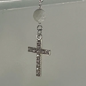 By prisförslag- 1 st Glittrigt korsörhänge med pärldetalj - Snyggt örhänge med ett glittrande kors i silverfärg, dekorerat med små stenar. Ovanför korset sitter en rund, vit pärlliknande detalj som ger extra stilpoäng. Perfekt accessoar för dig som vill sticka ut med en cool och trendig look. 1 st