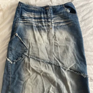 Lång jeanskjol med fransade detaljer - Cool lång jeanskjol i blått med slitna och fransade detaljer, snedsydd ficka och rå kant nertill. Kjolen har en unik tvättad look och en liten slits bak för extra rörelsefrihet. Perfekt för dig som gillar en edgy och avslappnad stil. Den är 100% bomull:)