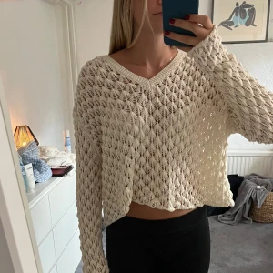 Beige stickad croppad tröja från Chiquelle - Superfin beige stickad tröja från Chiquelle med croppad passform och v-ringning. Tröjan har ett luftigt, hålmönstrat stickat material och långa ärmar. Perfekt att slänga på sig över ett linne eller bikini under varmare dagar.