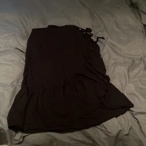 Svart omlottkjol  Pernilla Wahlgren - Svart omlottkjol från Pernilla Wahlgren Design i storlek 34. Kjolen har volang framtill knytband i midjan, knapp i tre olika lägen och en snygg guldig detalj vid sidan. Perfekt för dig som gillar stilrena och trendiga plagg.