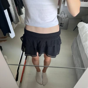 Svart volangkjol från Gina Tricot - Supersöt svart kortkjol från Gina Tricot i storlek 158-164. Kjolen är luftig och har en lätt, flowy känsla som passar perfekt till en snygg topp eller hoodie. Enkel att styla och riktigt skön att bära. Aldrig använd! 