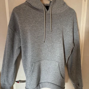 Grå hoodie från shein med huva - En klassisk grå hoodie från shein med huva och snörning. Tröjan har en stor känguruficka framtill och ribbade muddar vid ärmslut och nederkant. Perfekt för chill dagar eller när du vill ha en enkel och stilren look. Köpt på SHEIN för längesen så därför ser man inte på etiketten. I övrigt inga defekter och sitter bra. I stl M. Bara att höra av dig!🥰