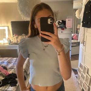 Ljusblå topp med volangärmar - Supersöt ljusblå topp med korta volangärmar och rund hals. Croppad modell som ger en fräsch vibe till outfiten. Tillverkad i mjuk, ribbad bomull som känns skön mot huden. Perfekt att styla med jeans eller kjol för en chill look.