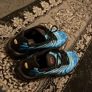 Tn nike Air Max Plus blå/röd sneakers riktiga skor - Nike Air Max Plus sneakers med blått mönstrat tyg, svarta detaljer och röda sidor med röd sula. Snyggt vågigt mönster och synlig Air Max-dämpning. Röd Swoosh-logga på sidan och TN-logga på hälen. Perfekta för dig som vill sticka ut.