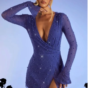 Blå glittrig kortklänning med pärlor  - Supersnygg blå kortklänning från OH polly med glittrande pärlor över hela tyget. Djup v-ringning, omlott framtill och långärmad modell. Klänningen har en liten slits och sitter tight för en riktigt festlig look. Perfekt för dig som vill sticka ut!