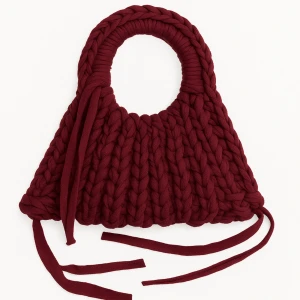 Vinröd stickad handväska med snörning - Superfin vinröd handväska i chunky stickat material med runda handtag och långa snören som detalj. Väskan har en cool, unik form och känns både trendig och mysig – perfekt för dig som vill sticka ut med accessoarerna.