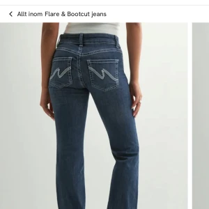 Blå bootcut jeans med broderade fickor - Snygga blå bootcut jeans med coola broderade bakfickor och dubbla knappar i midjan. Jeansen har klassisk femficksdesign, kontrastsömmar och är tillverkade i stretchig denim för en bekväm passform. 