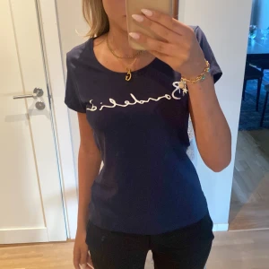 Mörkblå Bondelid t-shirt - Snygg mörkblå t-shirt från Bondelid med vit logga tryckt över bröstet. Modellen är klassisk med rund halsringning och korta ärmar. Skön passform och tillverkad i mjuk bomull, perfekt för en chill och stilren look. Använd en gång. 