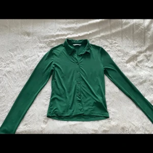 Grön skjorta från Stradivarius S - Snygg grön skjorta från Stradivarius i storlek S. Skjortan har klassisk krage, långa ärmar och knäppning framtill. Materialet känns mjukt och lätt, perfekt för en stilren look. Passar dig som gillar enkel men trendig stil.