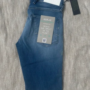 Replay Anbass Hyperflex jeans blå - Snygga Replay Anbass Hyperflex jeans i mellanblå tvätt. Jeansen är tillverkade i stretchigt denim och har klassisk femficksdesign, silverfärgade detaljer och tydliga sömmar. Perfekta för dig som vill ha både stil och komfort.
