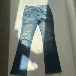 Blå bootcut jeans från Sama - Snygga blå jeans från Sama med bootcut passform och klassiska fickor. Jeansen har dekorativa detaljer på bakfickorna och en läderpatch med logga bak i midjan. 