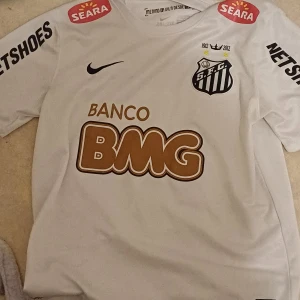 Vit Santos fotbollströja Neymar Jr #11 - Santos FC matchtröja i vitt med Neymar Jr och nummer 11 på ryggen. Tröjan har svarta tryck, sponsorer och klubbmärke på bröstet. Tillverkad i Dri-Fit material för bra ventilation. Klassisk passform och korta ärmar.