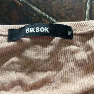 Ljusrosa ribbad linnetopp med spets från BikBok - Säljer en ljusrosa ribbad linnetopp från BikBok med justerbara axelband och spetsdetaljer längs urringningen. Perfekt att styla till jeans eller kjol för en söt och enkel look.