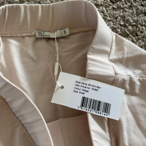 Beige midikjol från NLY Trend - Säljer en beige midikjol från NLY Trend i storlek S. Kjolen har en rak passform med resår i midjan och en liten slits på sidan. Perfekt för dig som gillar stilrena och enkla plagg.