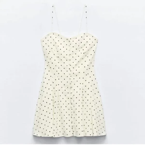 Vit prickig kortklänning med knappar och snörning - Supersöt vit kortklänning med svarta prickar och tunna axelband. Klänningen har knappar framtill och snörning i ryggen. 🖤🤍