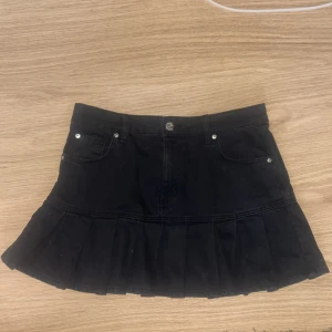 Svart low waist volangkjol från Bershka - Supersöt svart minikjol från Bershka med volang nertill och klassisk jeanslook. Kjolen har fickor fram och bak samt knapp och dragkedja i midjan. Perfekt för dig som gillar trendiga och feminina plagg.