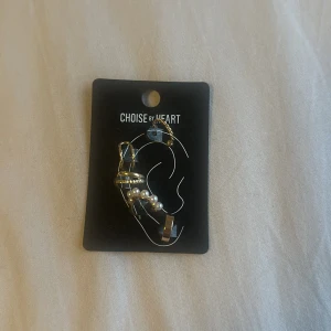 Guldörhängen med pärldetaljer från Choise by Heart - Säljer ett par unika guldörhängen från Choise by Heart med dekorativa pärlor och kedjedetaljer. Snygg och trendig design som ger en cool touch till din stil.