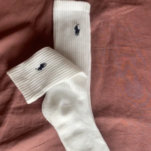 Vita strumpor från Polo Ralph Lauren - Säljer ett par klassiska vita strumpor från Polo Ralph Lauren med den ikoniska mörkblå loggan broderad på skaftet. Strumporna är ribbade upptill och har en mjuk och bekväm passform. Perfekta för en stilren vardagslook.