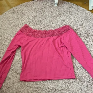 Rosa offshoulder topp med spets  - Säljer en snygg rosa offshoulder topp från Pieces i storlek XL. Toppen har långa ärmar, ribbad struktur och en bred spetskant upptill som ger en romantisk känsla. Perfekt för dig som vill sticka ut med färg och detaljer!