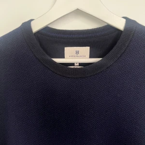 Mörkblå stickad tröja från Hansen & Jacob - Säljer en stilren mörkblå stickad tröja från Hansen & Jacob i merino cotton blend. Tröjan har rund halsringning och diskret logga broderad vid halsen. Perfekt för lager-på-lager och passar till många olika outfits. Använd under 5 gånger. 