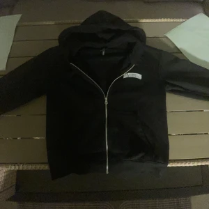 Svart hoodie med dragkedja från H&M - Svart hoodie från H&M med dragkedja och huva. På bröstet står det 'LA Privileges' i vitt tryck och på ryggen finns ett större tryck med samma text. Modellen är loose fit och har långa ärmar.