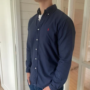 Marinblå Ralph lauren skjorta  - Säljer denna feta Ralph lauren skjorta i marinblått med röd logga, den är i mycket bra skick den är i storlek medium modell slim fit med 75 cm längd och 52 cm bredd under armhålorna, hör gärna av dig vid frågor! 