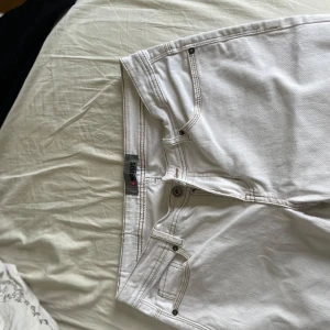 Vita jeansbyxor från Mards - Säljer ett par klassiska vita jeansbyxor från Mards med fickor och silverfärgade nitar. Byxorna har normal passform och bootcut , perfekta för en stilren look. Tidlös design med diskreta sömmar och logga på bakfickan. Storlek M men passar S