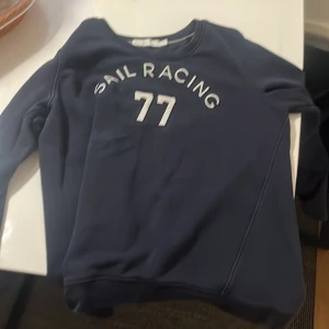 Marinblå sweatshirt från Sail Racing - Säljer en marinblå sweatshirt från Sail Racing med vitt tryck 'SAIL RACING 77' Har inte använt tröjan den står M på den fast den passar runt S 
