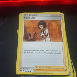 Cara Liss - Pokémonkortet 'Cara Liss' är en supporter-tränare som hjälper dig att hitta Rare Fossil-kort till din bänk. Perfekt för samlare och spelare som gillar strategiska drag i Pokémon TCG.
