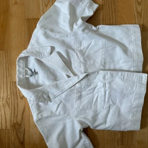 Vit kortärmad jeansjacka från erica kvam x NAKD - Vit kortärmad jeansjacka från erica kvam x NAKD med korta ärmar och klassisk krage. Jackan har två bröstfickor och knappar framtill. modellen är lite boxig och croppad.