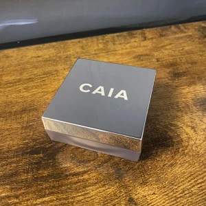 CAIA Loose Setting Powder Honey Glow - Löspuder från CAIA i nyansen Honey Glow. Kommer i en stilren fyrkantig förpackning med spegelblankt lock och tydlig logga. Puderfärgen är varm och gyllene, perfekt för att fixera sminket och ge en glowig finish. Använd fåtal gånger 