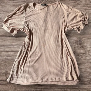 Ljusrosa ribbad topp med puffärm från MyWear Woman - Säljer en ljusrosa ribbad topp från MyWear Woman i storlek L. Toppen har korta puffärmar och rund halsringning. Materialet är mjukt och stretchigt, perfekt för en avslappnad men ändå trendig look.