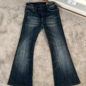 Mörkblå bootcut jeans från Crocker - Säljer ett par mörkblå bootcut jeans från Crocker, modell Pow Flare. Jeansen har klassisk femficksdesign, normal passform upptill och utsvängda ben. Snygga slitningar och detaljer i guldtråd. Perfekta för dig som gillar retrostil!