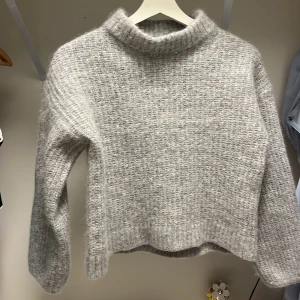 Ljusgrå stickad tröja från Stockh LM - Supermjuk och mysig ljusgrå stickad tröja från Stockh LM. Tröjan har en hög krage, lång ärm och en lätt croppad passform. Perfekt för lager-på-lager och enkel att matcha med olika outfits. Skulle säga att den är xxs då den krympte i tvätten även om det står xs.