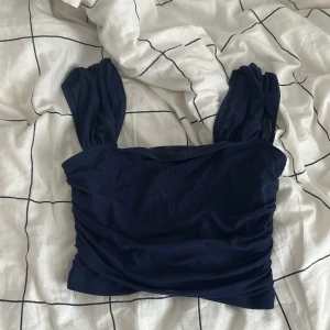 Mörkblå topp med puffärmar från SHEIN - Säljer en mörkblå topp från SHEIN med breda puffärmar och rynkade sidor. Toppen har en croppad passform och är tillverkad i ett lätt, syntetiskt material. Perfekt för att skapa en trendig look 💘💘