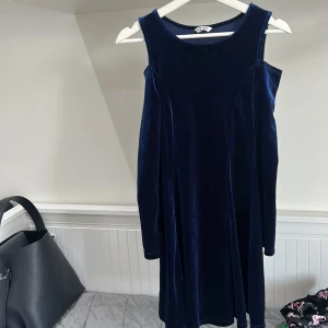 Mörkblå sammetklänning med cold shoulder - Säljer en snygg mörkblå klänning i sammet med cold shoulder-design och breda axelband. Klänningen har en mjuk känsla och är perfekt för dig som gillar en stilren men trendig look.